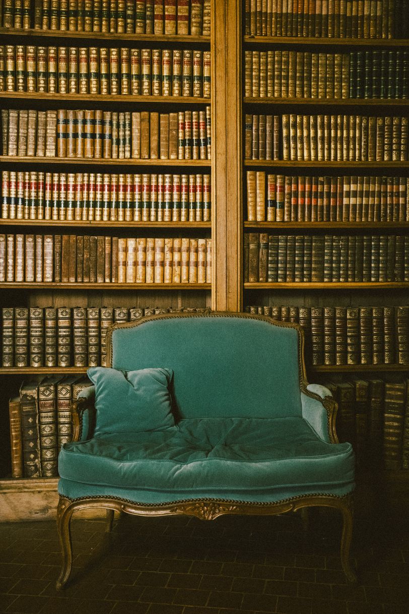 A bookcase full of old books behind an old armchair obviously used
