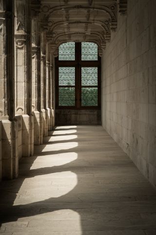 Half enlighted stone corridor in a castle with a window at the end