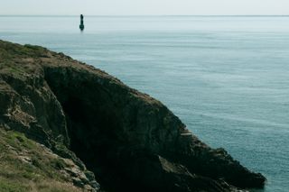 Seascape with a cliff on the foreground and a lone lighthouse lost at sea in the background