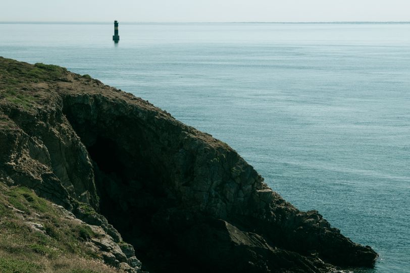 Seascape with a cliff on the foreground and a lone lighthouse lost at sea in the background