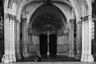 A beggar sitting under the front arches of a church