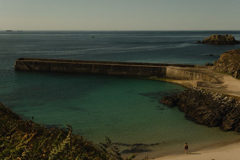 Small beach with a stone dock and a single person walking on the sand