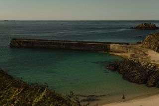 Small beach with a stone dock and a single person walking on the sand