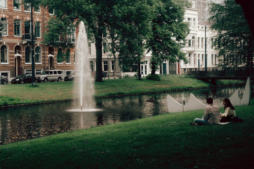 A couple sitting and chatting on the edge of a river in town from which a geyser emerges