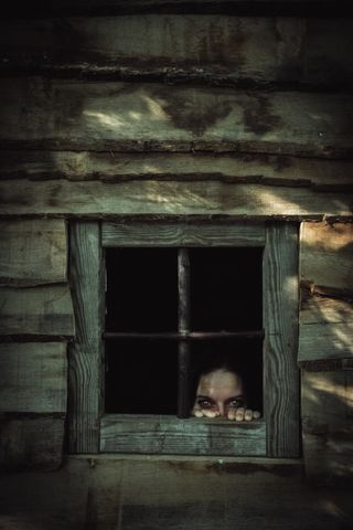 A creepy face showing from the window on an old wood cabin