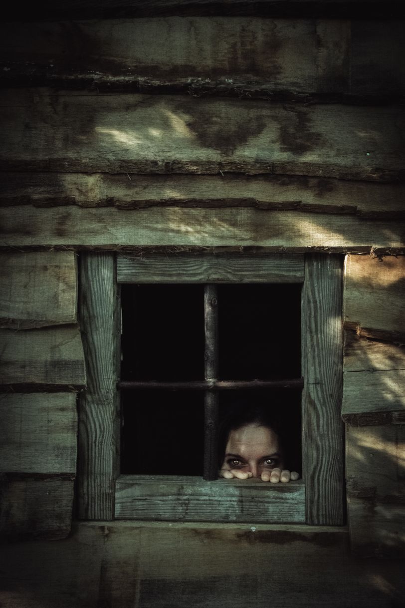 A creepy face showing from the window on an old wood cabin