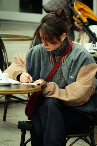 A young woman sitting at a café and writing down on a notebook