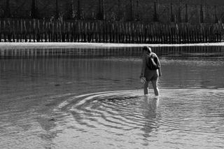 A woman walking in the water, creating circles, while in the back are only vertical lines
