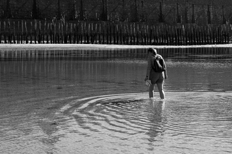 A woman walking in the water, creating circles, while in the back are only vertical lines