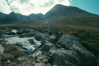 Stream of water running in a green prairie with mountains in the background