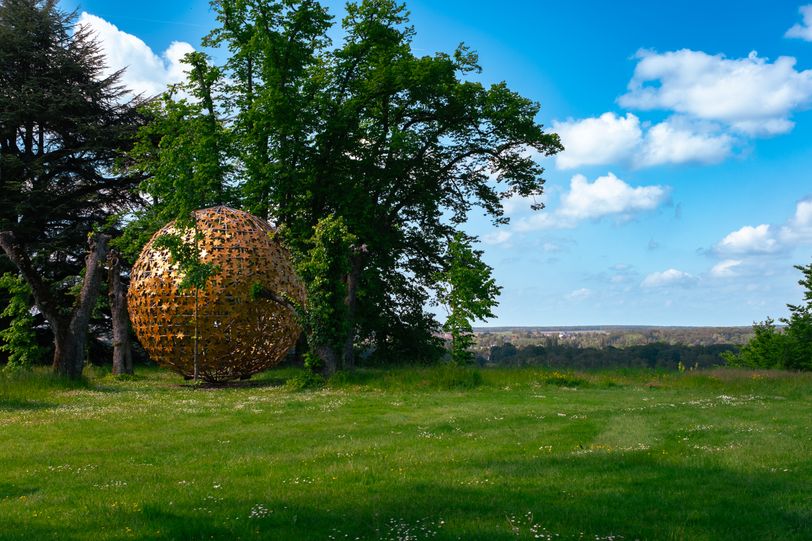 Golden sculpture showing leaves making a ball in a garden
