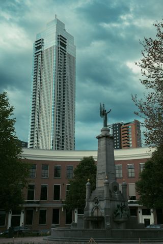 A tall modern building in the background and a small monument in the foreground