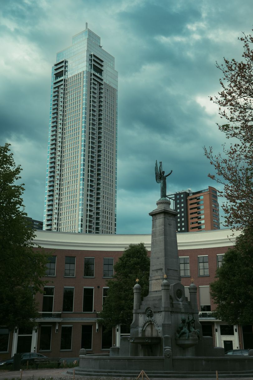 A tall modern building in the background and a small monument in the foreground