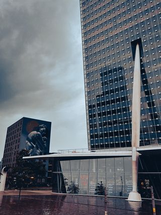 View of city buildings that appear distorted. On one of them there is a paiting on one side and the other has a pole keeping it straight