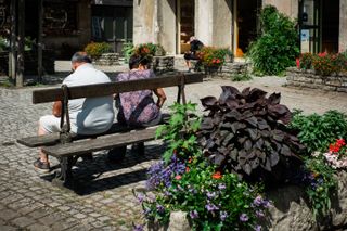 People sitting on benches in the middle of a village on a sunny day