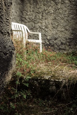 Plastic chair in a corner of a stone structure overgrown with wild flora