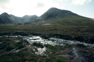 Moutains in the background with the sun behind them and a small water stream in the foreground and nothing else in between