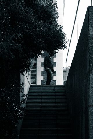 Black and white picture from below of a man walking by the top of the stairs