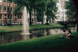 A couple sitting and chatting on the edge of a river in town from which a geyser emerges