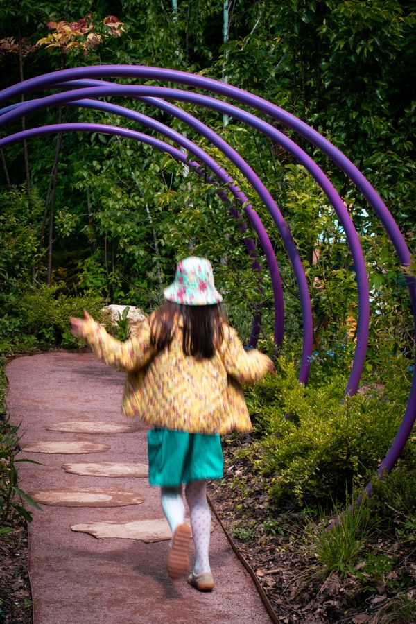 A young girl hopping through purple circles on a dirt path in a garden