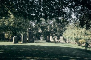 View on a cemetery park with old large tombstones and people sitting and chatting in a sunny weather