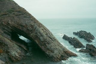 Leaning cliff on a rainy day with massive hole in it