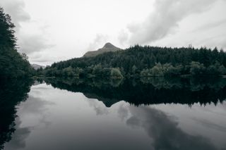 Landscape of a lake surrounded by a forest with a mountain in the background which looks like a head of a person lying down