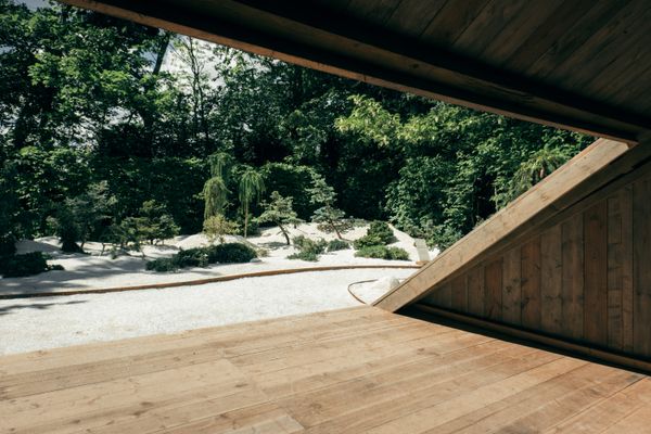 A human made shelter, in straight wood planks, in front of a garden with white sand all over the floor