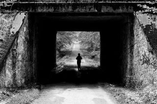 Black and white picture of a dark passage under a road with someone walking under it