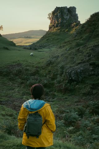 Landscape of a rock formation in golden hour behind a grazing sheep and the back of a person in the foreground enjoying the landscape