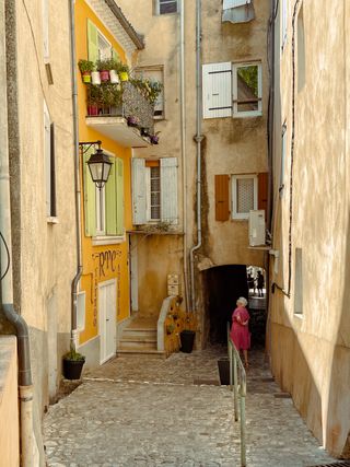 An old lady in a yellow street watching at some Tattoo shop