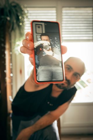 Portrait of a man holding a phone to the camera displaying a portrait of the photographer taking the portrait shot