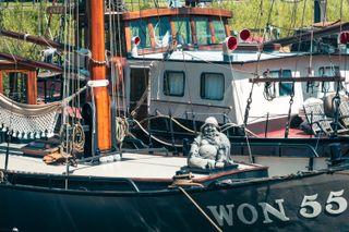 Close up on sailing boat with a statue of Buddha on deck wearing a sailor hat on its head