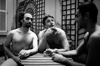 Three nude men around a table taking a break