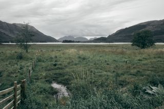 View of a meadow in the foreground and a loch and mountains in the background