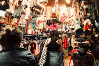 View of inside a thrift shop where a dummy acrobat is hanging from the ceiling above a client who's just looking for clothes