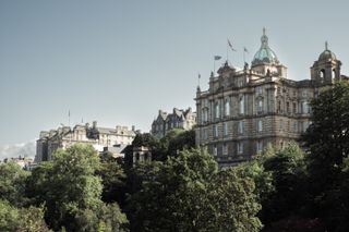 Old building in the heights of Edinburg with trees below it.