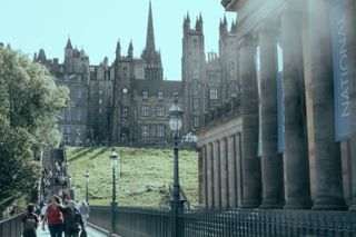 View on a crowded touristic walkway in the center of Edinburgh with old buildings in the background and a majestic building with columns on the side