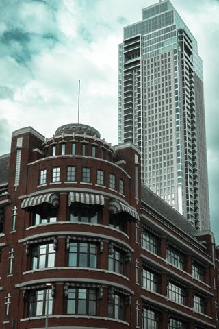 Two very different building in Rotterdam, a short old one with red bricks and round corners, a tall new one mostly of glass with sharp corners behind the first one.