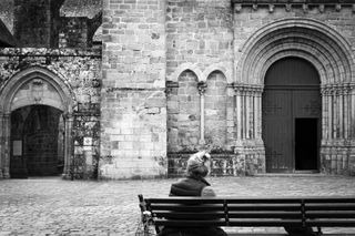 A person sitting on a bench facing two entrances from old buildings