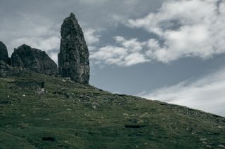 Erected rock on a grassy inclined plan and a blue sky with some white clouds in the background