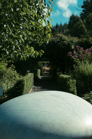 View of a passageway in a wall maintained garden with a gigantic stone in the foreground at the bottom of the picture