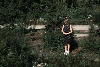 A little girl standing still and staring at a pond in a garden