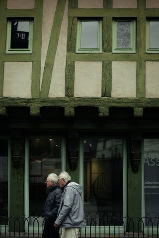 Two older men walking in the streets in front of a green shop