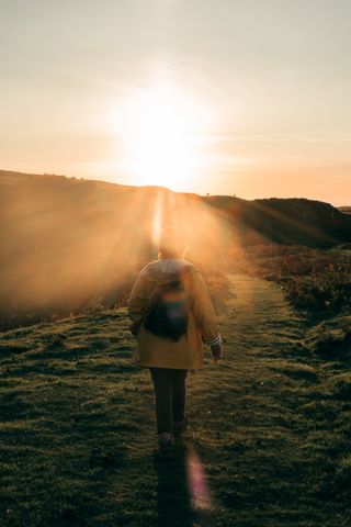 A female silhouette walking on a hilly terrain to the setting sun