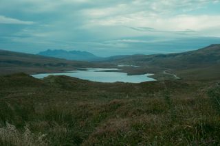 A loch in the hollow of a valley with a mountain in the background on a misty morning