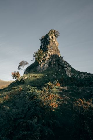 Cone shaped rock covered in grass and bushes on a setting sun