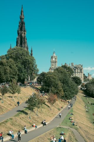 Sunny day in a park in Edinburgh with people enjoying the sun either by walking or laying on the grass