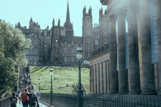 View on a crowded touristic walkway in the center of Edinburgh with old buildings in the background and a majestic building with columns on the side