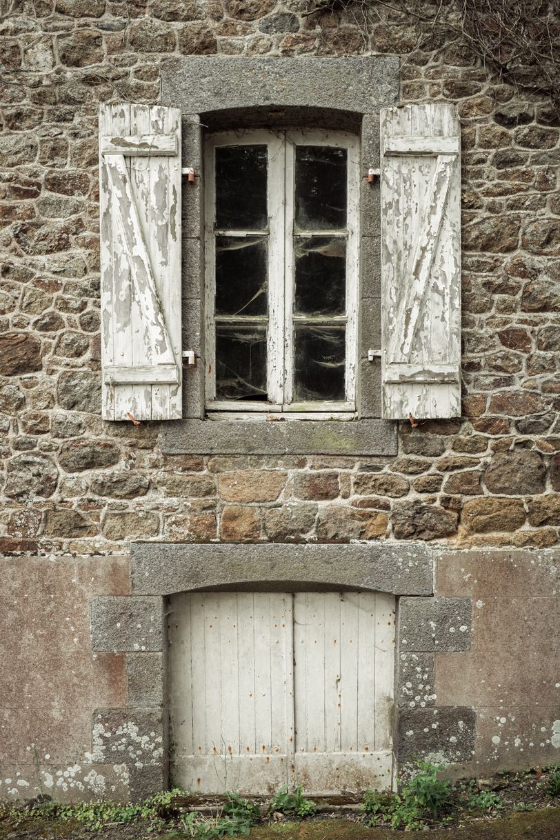 Facade of an old house with a basement hatch and a window with cobwebs
